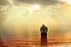 Imagen de un hombre dentro del mar frente al amanecer inclinado orando